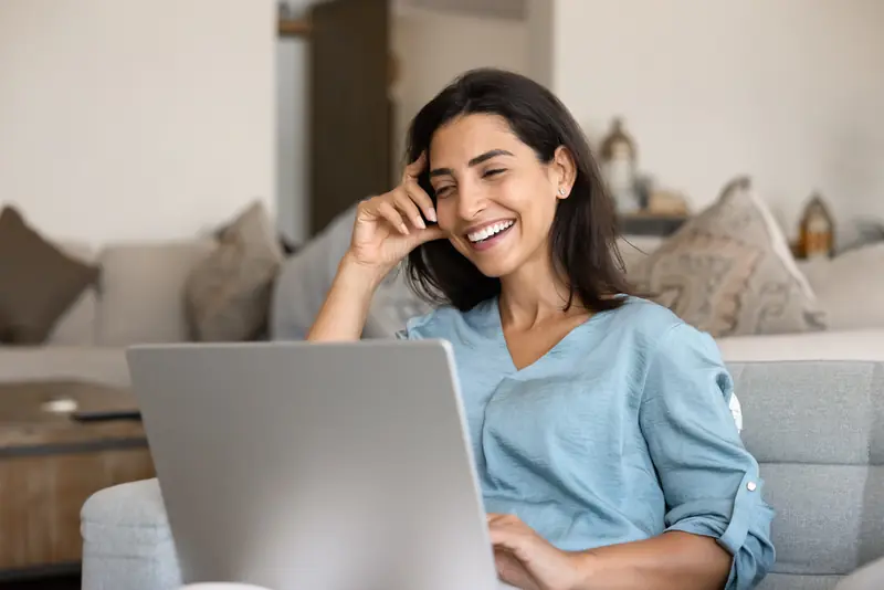 Frau sitzt mit ihrem Laptop auf dem Sofa und lacht